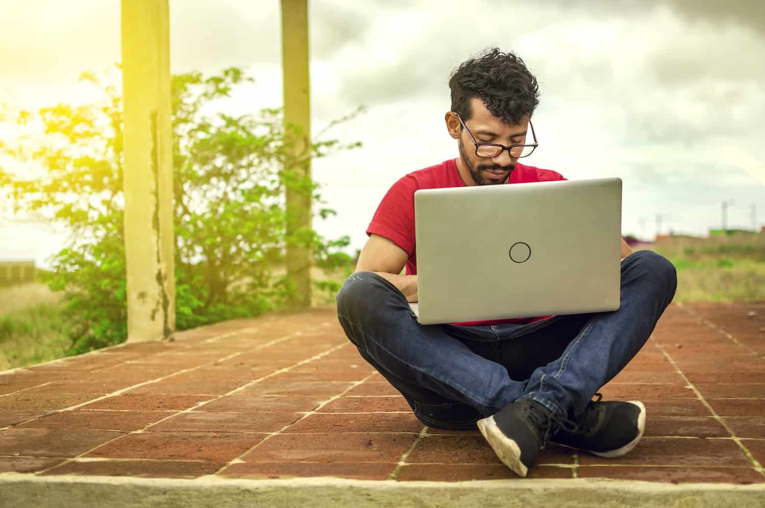 a man sitting cross legged on a brick floor using a laptop